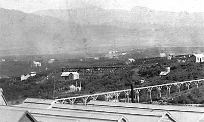 Cassels water race flume can be seen in the centre. The flume in the foreground is from the same source, but taking (excess?) water to the Waihi Mill. Note Silverton Battery in mid background. (photo before 1902). Note low vegetation only (teatree and bracken fern?) 