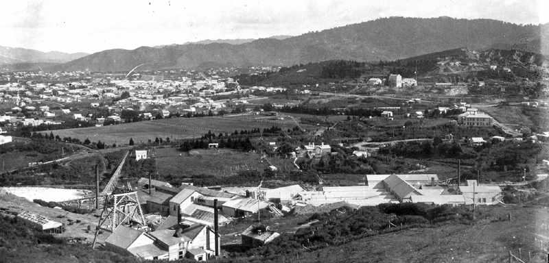 View from Union Hill overlooking the Waihi Battery, and much of the ground now traversed by Mill Stream Walkway. Middle left is the Recreation ground (now known as Morgan Reserve) with Baker Street on its left hand edge. The water race pipe taking the water captured from Mill Stream to the battery is visible, the original tennis courts and shelter are nearer the centre of the picture. The Battery managers house is clear at centre, and to the right of that the driveway into the quarry. The large building at middle right is the New Central Hotel, on the corner of Kenny Street and Barry Road, where the children's' playground is now. Martha Hill with Cornish Pumphouse top right. Photo c.1906, ATL 19313.